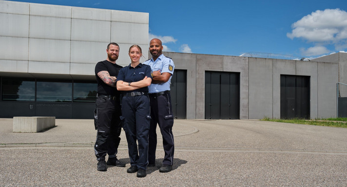 Justizvollzug Berufsperspektive Zwei Justizvollzugsbeamte und ein Werkdienstbeamte stehen vor einer Justizvollzugsanstalt